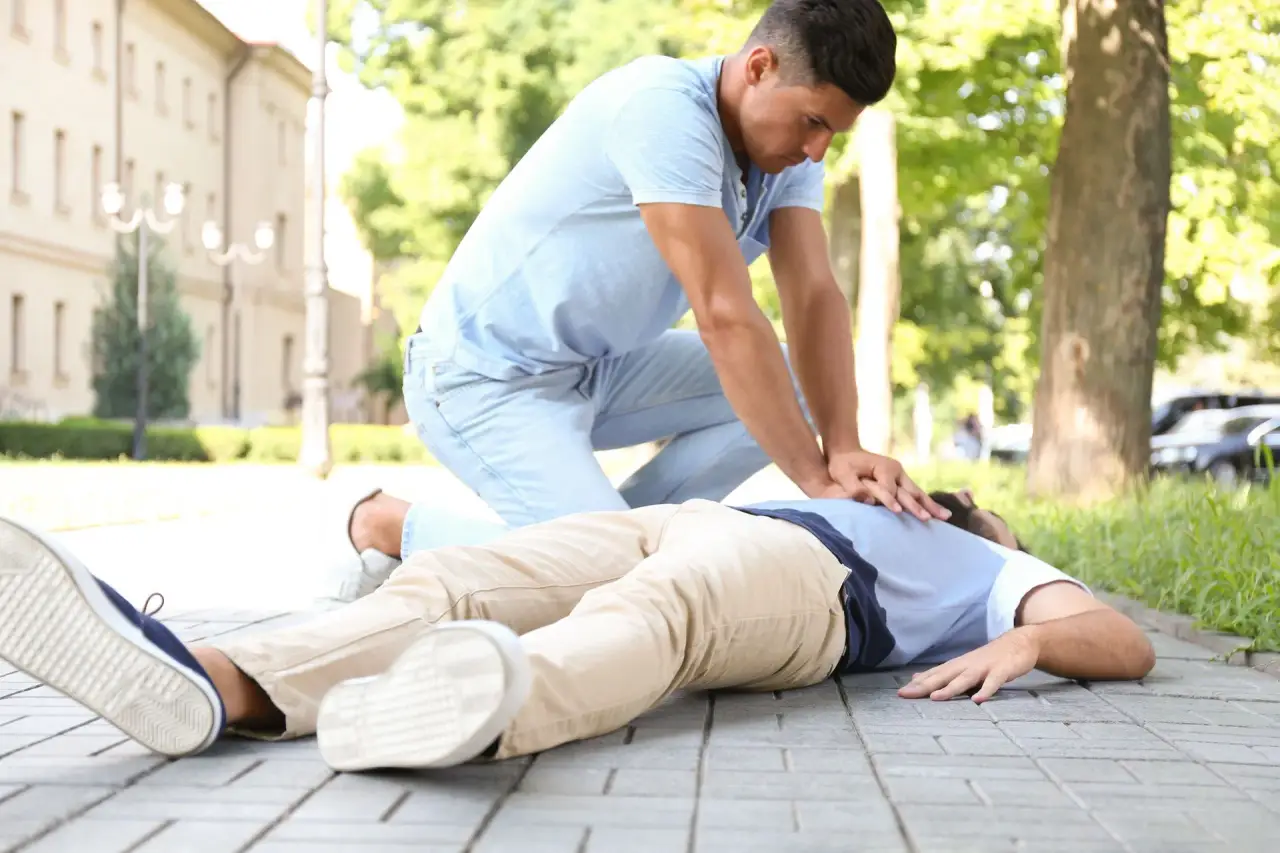 Person in light blue shirt performing chest compressions on someone lying on grass.