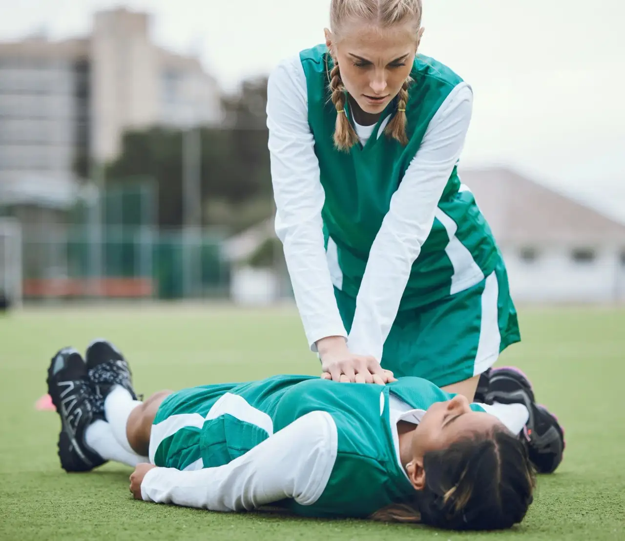 Person in white shirt and green vest outdoors on a sports field (top cropped).