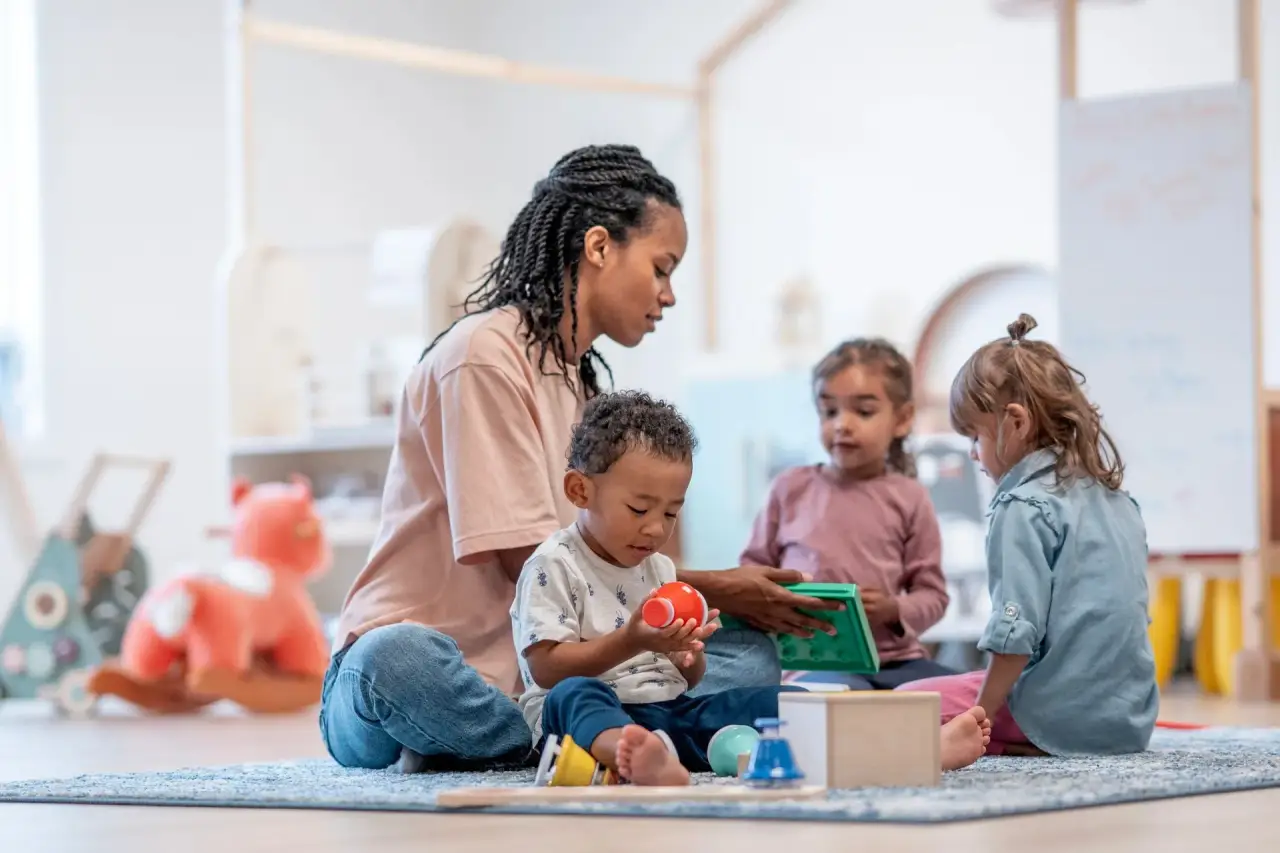 Caregiver sitting with a toddler playing with toys (childcare setting).
