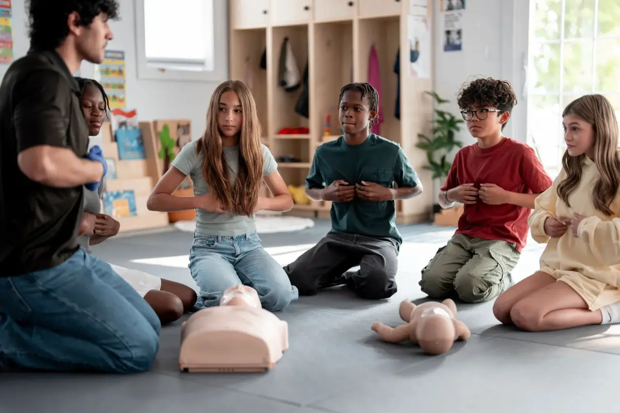 People sitting/kneeling outdoors practicing chest compressions on a person.