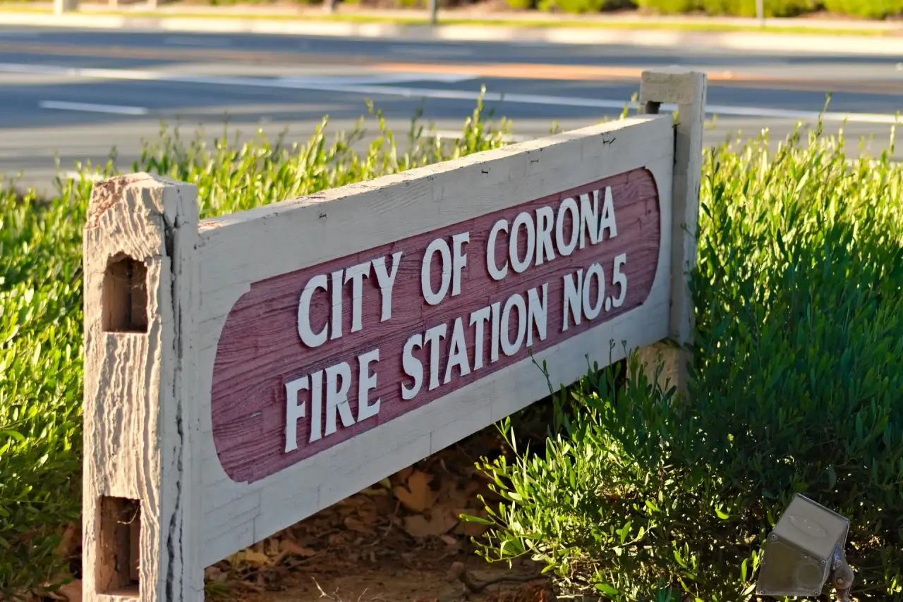 Wooden sign reading CITY OF CORONA FIRE STATION No.5 among greenery.